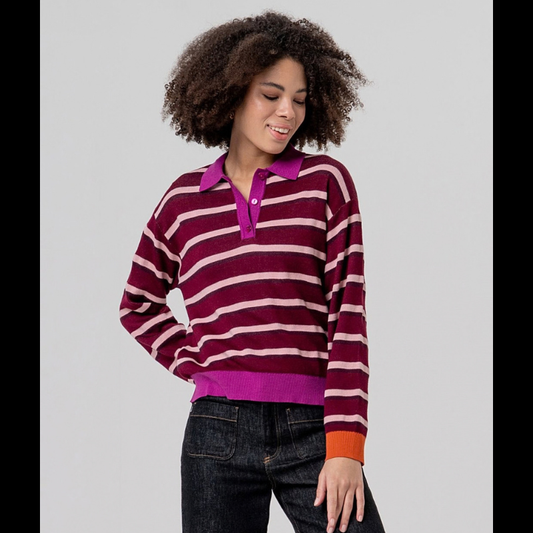 Camisola de malha de manga comprida com gola em polo com três botões. Camisola listrada com grená, rosa claro e bordô. Punhos a terminar em laranja e cós e gola em rosa forte.