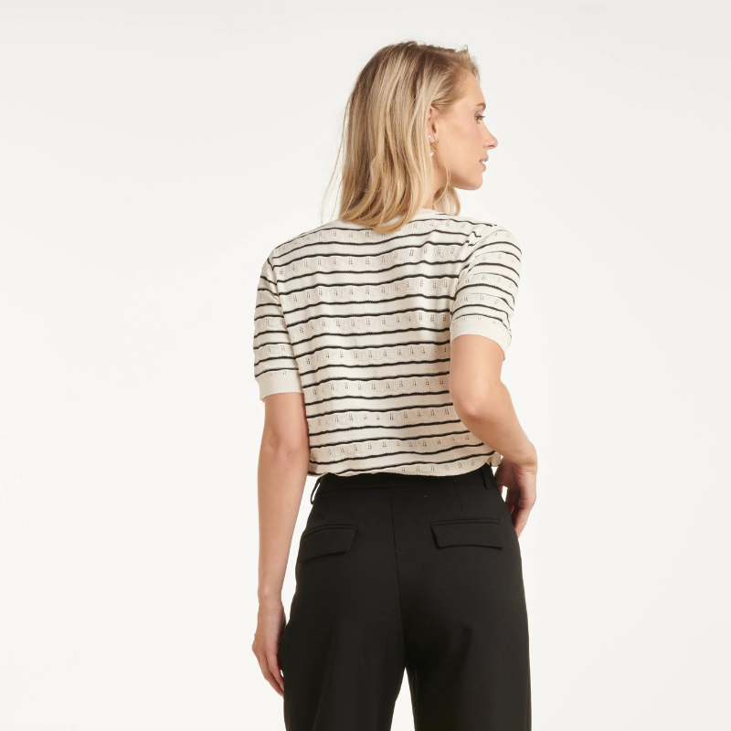 T-shirt de malha de manga curta em branco com riscas pretas. Pormenores de malha perfura na zona branca. Corte clássico com decote em V que oferece um visual elegante e versátil. Perfeita para combinar com qualquer look do dia a dia, esta peça é um essencial do guarda-roupa que funciona tanto em looks casuais como em composições mais sofisticadas.