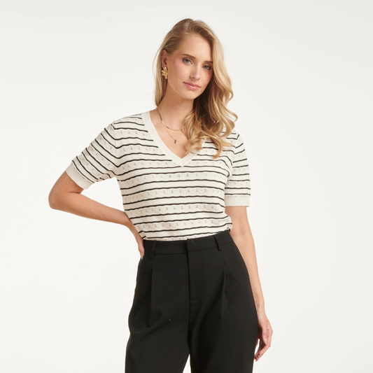 T-shirt de malha de manga curta em branco com riscas pretas. Pormenores de malha perfura na zona branca. Corte clássico com decote em V que oferece um visual elegante e versátil. Perfeita para combinar com qualquer look do dia a dia, esta peça é um essencial do guarda-roupa que funciona tanto em looks casuais como em composições mais sofisticadas.