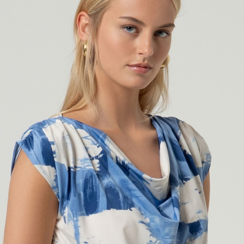 Descubra a elegância desta blusa sem mangas com decote drapeado sofisticado na frente e ombros delicadamente caídos. O corte reto oferece um ajuste perfeito ao corpo, realçando a sua silhueta de forma natural. Apresenta uma estampagem vibrante em tons de azul e branco que traz movimento e personalidade ao visual. A sua confeção combina sustentabilidade com conforto e flexibilidade para o seu dia a dia.