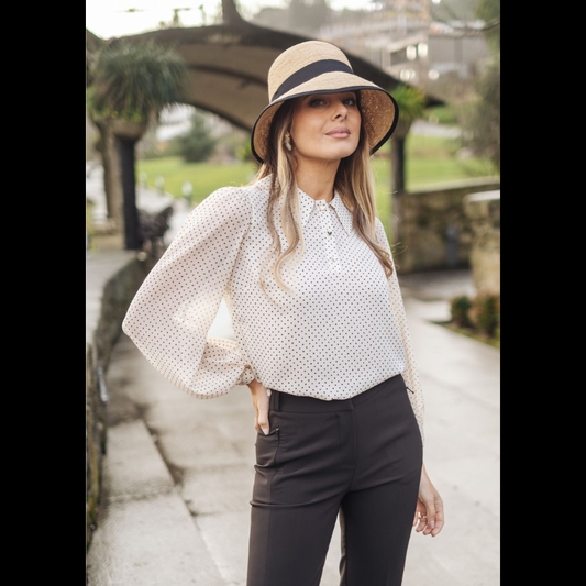 Túnica com estampado de bolinhas pretas sobre fundo bege/pérola. O colarinho tipo polo e a carcela frontal com três botões em formato coração conferem um toque delicado e refinado ao design. As mangas compridas em tecido transparente proporcionam leveza visual, enquanto o corpo apresenta um cair suave que acompanha naturalmente o movimento. Túnica versátil e elegante, adequada tanto para ambientes profissionais como para momentos mais descontraídos.