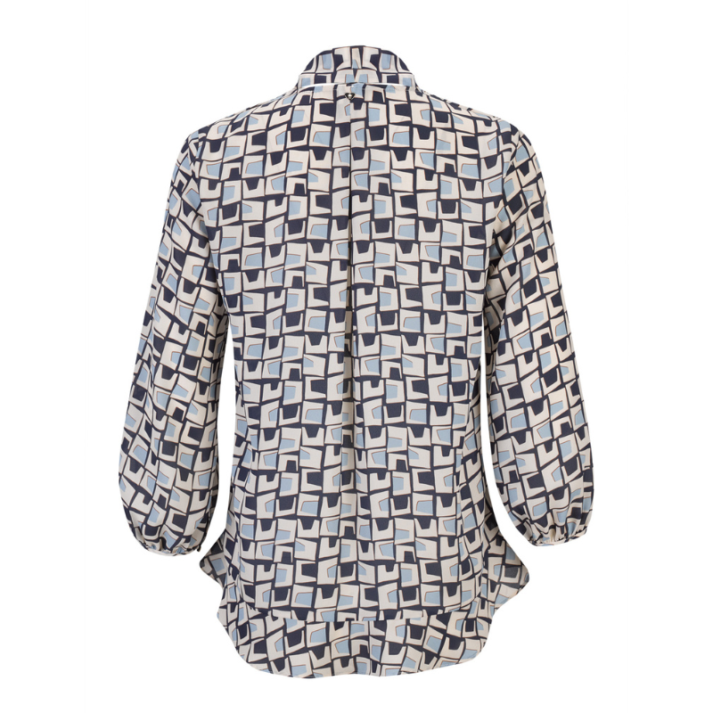 Túnica com decote em V em estampado geométrico nos tons de azul marinho e creme que combina sofisticação e modernidade com um toque de criatividade, perfeita para coordenar com tons neutros para looks equilibrados ou com jeans para um visual casual-chic.
Túnica com assimetria do comprimento, mais comprida atrás do que à frente e com aplicação de folhos o que reforça o carácter contemporâneo da peça e acrescentam movimento e leveza ao design. O destaque vai para a laçada amovível no pescoço, no mesmo te