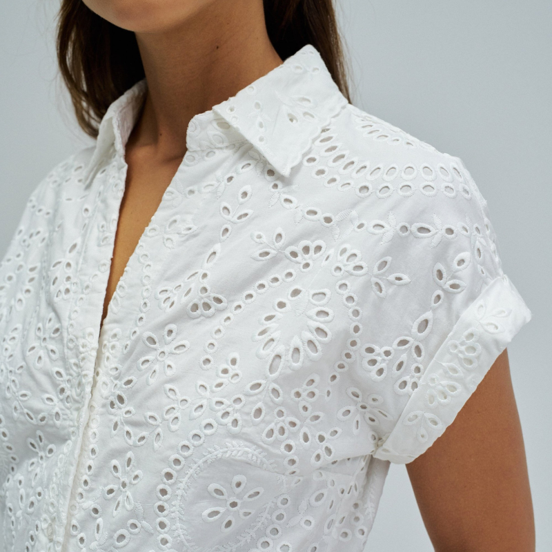 Vestido camiseiro em bordado inglês branco, perfeito para um look elegante e sofisticado. Apresenta manga curta, abertura frontal com botões e comprimento midi que favorece qualquer silhueta. Equipado com cinto removível para ajustar o caimento conforme deseja, bolsos funcionais e forro interior para maior conforto. Uma peça versátil que combina com facilidade no seu guarda-roupa do dia a dia.