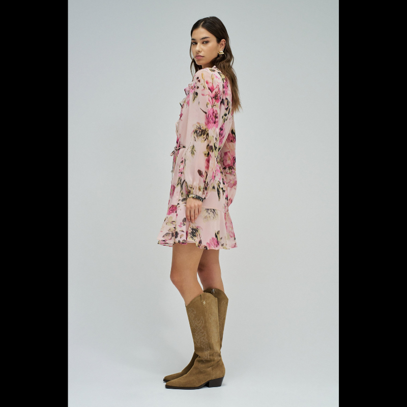 Vestido em tons rosa com padrão floral que combina elegância e movimento. O decote em V é realçado por folhos delicados, enquanto as mangas compridas apresentam punhos abotoados para um acabamento refinado. Destaca-se o cinto com pendentes nas extremidades, que adiciona dinamismo à silhueta. O folho na bainha confere volume e feminilidade. Vestido totalmente forrado para conforto e durabilidade. Uma peça versátil que transita com facilidade entre ocasiões casuais e mais sofisticadas.