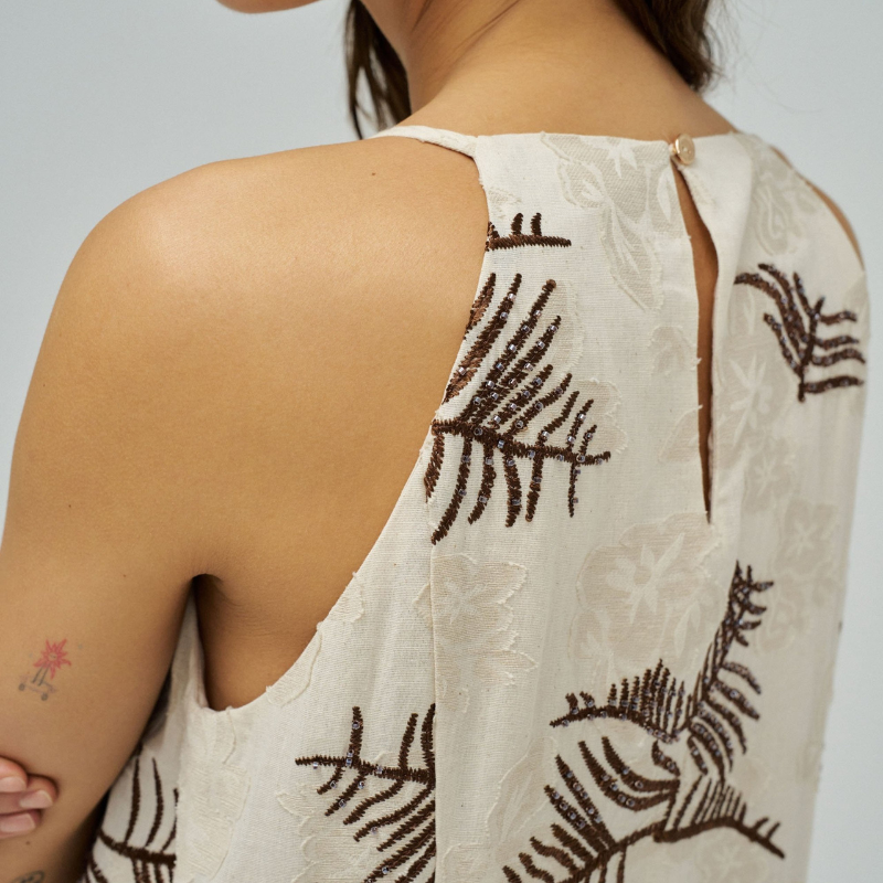 Vestido midi elegante em tons bege e castanho, perfeito para ocasiões especiais. Destaca-se pelos delicados bordados e missangas que adornam o tecido, criando um efeito sofisticado e refinado. Apresenta manga cava que oferece conforto e liberdade de movimento, com decote redondo clássico e feminino. Os bolsos funcionais adicionam praticidade ao design. A abertura nas costas com botão é um detalhe que confere sensualidade e movimento à peça. Ideal para eventos, jantares ou encontros especiais onde deseja des