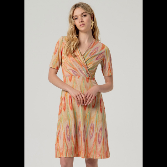 Vestido curto e de manga curta em malha fina que combina elegância e movimento. O decote em V e o fecho em traspasse no peito criam uma silhueta refinada e lisonjeira. O padrão geométrico em tons quentes—vermelho, laranja e verde—destaca-se sobre a base bege neutra, enquanto os fios de Lurex dourado adicionam um toque de sofisticação e luminosidade. Uma escolha contemporânea para quem valoriza detalhes bem executados e design atemporal.