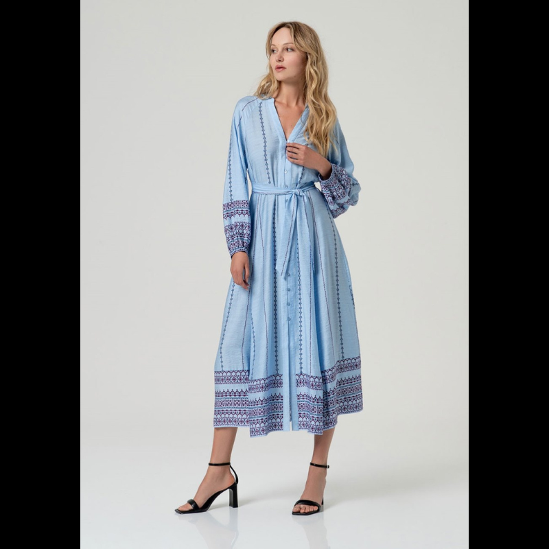 Vestido camiseiro midi em azul com cintura marcada e decote em V elegante. Mangas compridas com elástico nos punhos e detalhes de bordado geométrico em marinho e bordô. Faixa bordada na barra e nos punhos adiciona sofisticação. Fecha na frente com botões em azul claro e vem acompanhado por um cinto do mesmo tecido e padrão. Peça versátil perfeita para o dia a dia com um toque de refinamento.