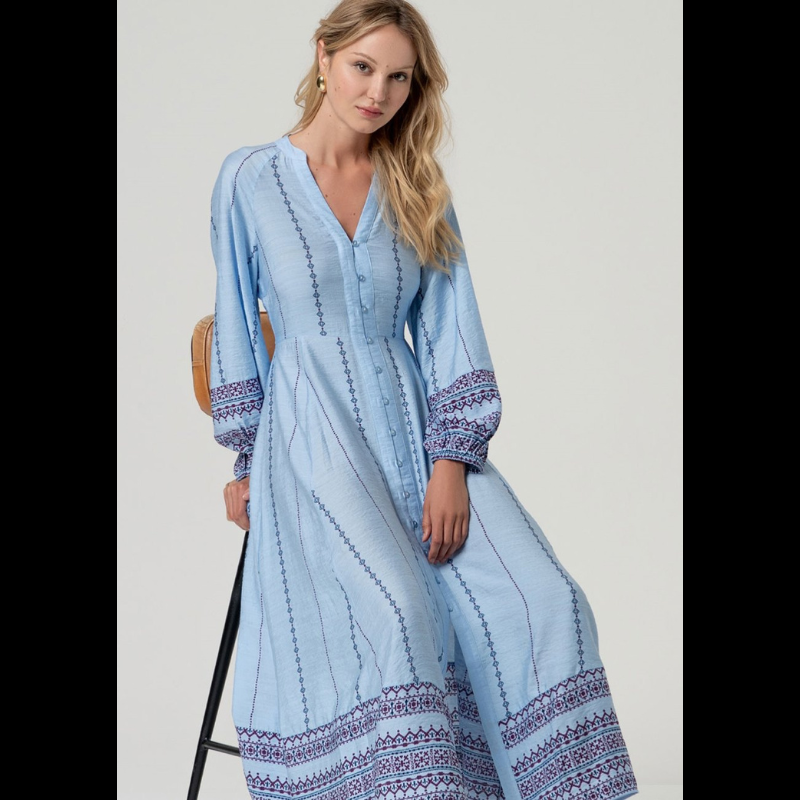 Vestido camiseiro midi em azul com cintura marcada e decote em V elegante. Mangas compridas com elástico nos punhos e detalhes de bordado geométrico em marinho e bordô. Faixa bordada na barra e nos punhos adiciona sofisticação. Fecha na frente com botões em azul claro e vem acompanhado por um cinto do mesmo tecido e padrão. Peça versátil perfeita para o dia a dia com um toque de refinamento.