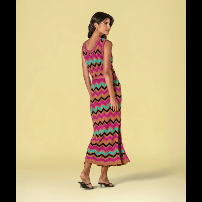 Vestido versátil em malha com decote redondo e cavas generosas, apresentando um padrão geométrico em zigzag que combina fúcsia, caramelo, verde-água e preto. O corte midi é complementado por duas aberturas laterais que conferem movimento e conforto. Inclui cinto coordenado nos mesmos tons, permitindo ajustar o caimento conforme desejado. Uma escolha sofisticada para quem valoriza design contemporâneo e funcionalidade.