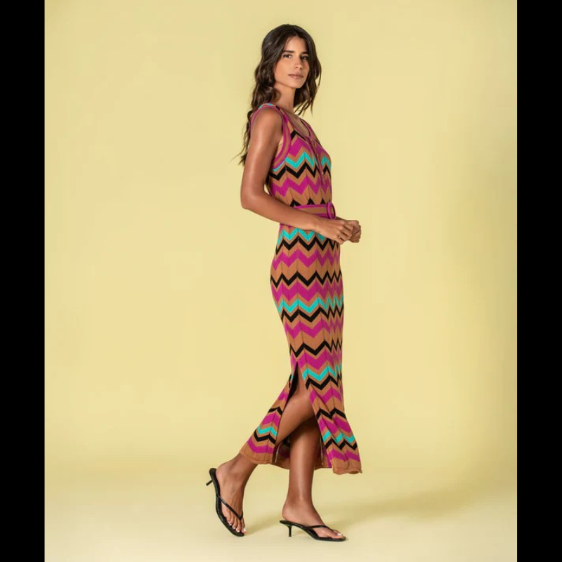 Vestido versátil em malha com decote redondo e cavas generosas, apresentando um padrão geométrico em zigzag que combina fúcsia, caramelo, verde-água e preto. O corte midi é complementado por duas aberturas laterais que conferem movimento e conforto. Inclui cinto coordenado nos mesmos tons, permitindo ajustar o caimento conforme desejado. Uma escolha sofisticada para quem valoriza design contemporâneo e funcionalidade.