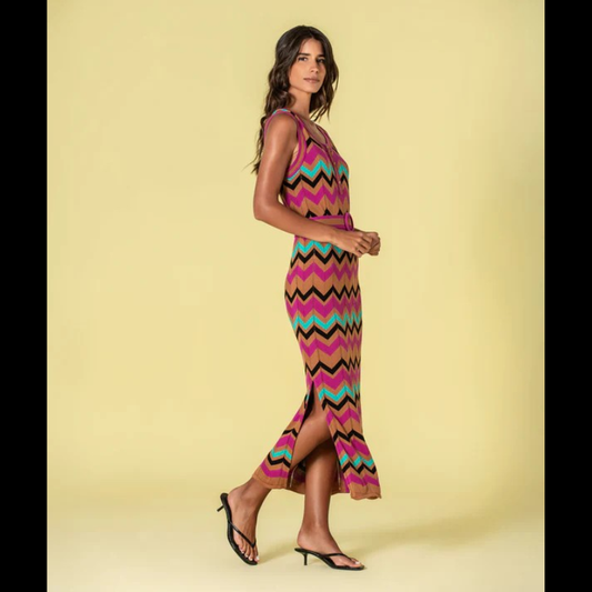 Vestido versátil em malha com decote redondo e cavas generosas, apresentando um padrão geométrico em zigzag que combina fúcsia, caramelo, verde-água e preto. O corte midi é complementado por duas aberturas laterais que conferem movimento e conforto. Inclui cinto coordenado nos mesmos tons, permitindo ajustar o caimento conforme desejado. Uma escolha sofisticada para quem valoriza design contemporâneo e funcionalidade.