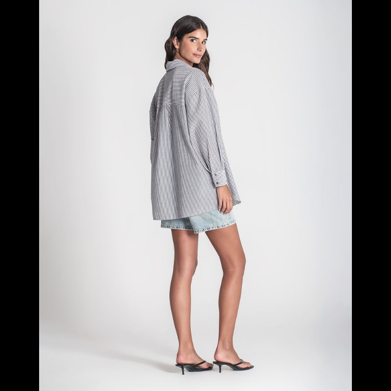 Camisa "oversize" de manga comprida às riscas brancas e cinza. Camisa a fechar na frente e punhos com botões cinzentos. Abertura nas laterias
Composição: 65%Poliéster + 35%Algodão
